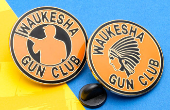 Two orange and black lapel pins for the Waukesha Gun Club featuring a shooter silhouette and a feathered headdress logo.