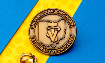 Antiqued gold lapel pin for University of Cincinnati Veterinary Technology featuring an Ohio state outline and veterinary symbol.