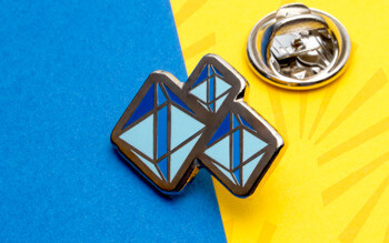 Geometric lapel pin featuring blue and light blue faceted diamond shapes with a silver butterfly clutch backing.