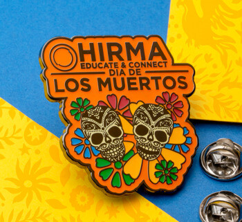 Orange and black HIRMA Dia de Los Muertos lapel pin featuring two decorated sugar skulls and colorful flowers.