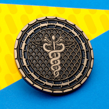 Challenge coin featuring a gold caduceus over a chain-link fence background, encircled by a barbed wire border on a black field.