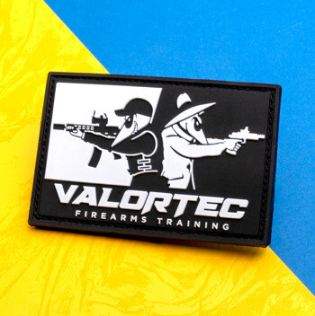Rectangular PVC patch featuring the Valortec logo and two characters with firearms against a black and white background.