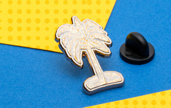 Polished silver palm tree lapel pin with a black rubber clutch on a yellow and blue background.