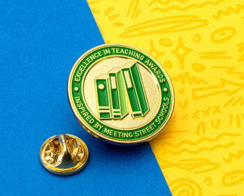 Gold and green Excellence in Teaching Awards lapel pin featuring three green binders, inspired by Meeting Street Schools.