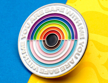 Circular lapel pin with rainbow and transgender flag colors featuring the text You Are Safe With Me.