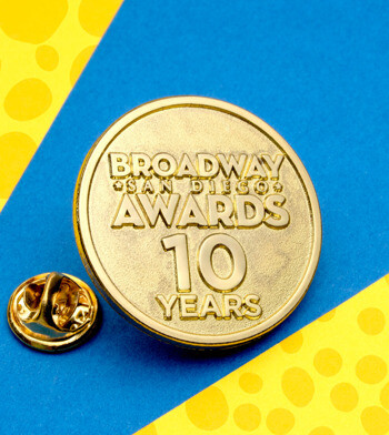 Gold circular lapel pin for Broadway San Diego Awards 10 Years, featuring raised lettering on a textured background with a butterfly clutch back.