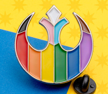 A lapel pin featuring the Starbird symbol filled with progressive pride flag colors, shown against a blue and yellow background.